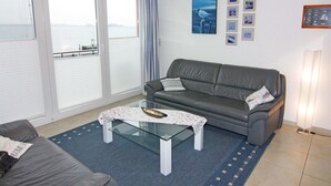 Una sala de estar con un sofá gris, una mesa de centro de vidrio y vistas al mar a través de amplios ventanales.