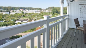 Un balcon donnant sur la ville, avec une balustrade blanche et un fauteuil en osier.