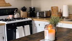 Una cocina con estufa, cafetera, tostadora y una vela sobre la encimera.