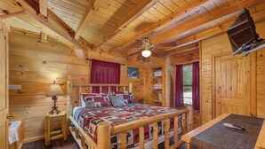 Quarto de cabana de madeira com uma cama, uma mesa de cabeceira, uma mesa e um ventilador de teto.