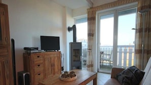 A cozy living room with a wooden table, a sofa, a television, and a fireplace. - Exklusives Appartement in Rechlin (Rechlin)