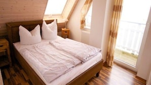 A bedroom with a wooden bed, white bedding, a nightstand, a lamp, and a window with curtains. - Exklusives Appartement in Rechlin (Rechlin)