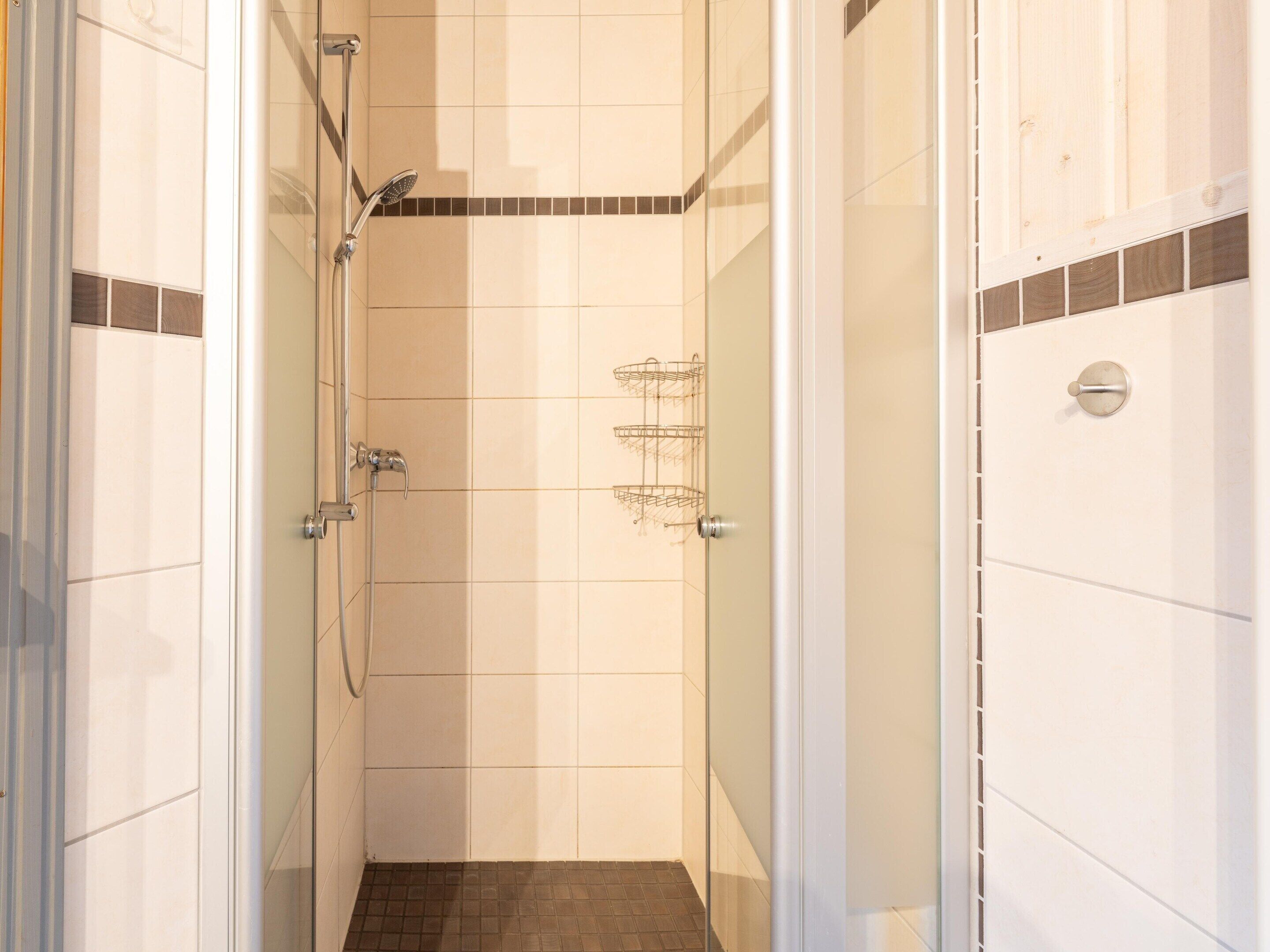 A narrow shower area with a glass door, tiled walls, and a showerhead.