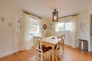 A dining area with a wooden table and chairs, a chandelier, and a view of the outdoors through windows.