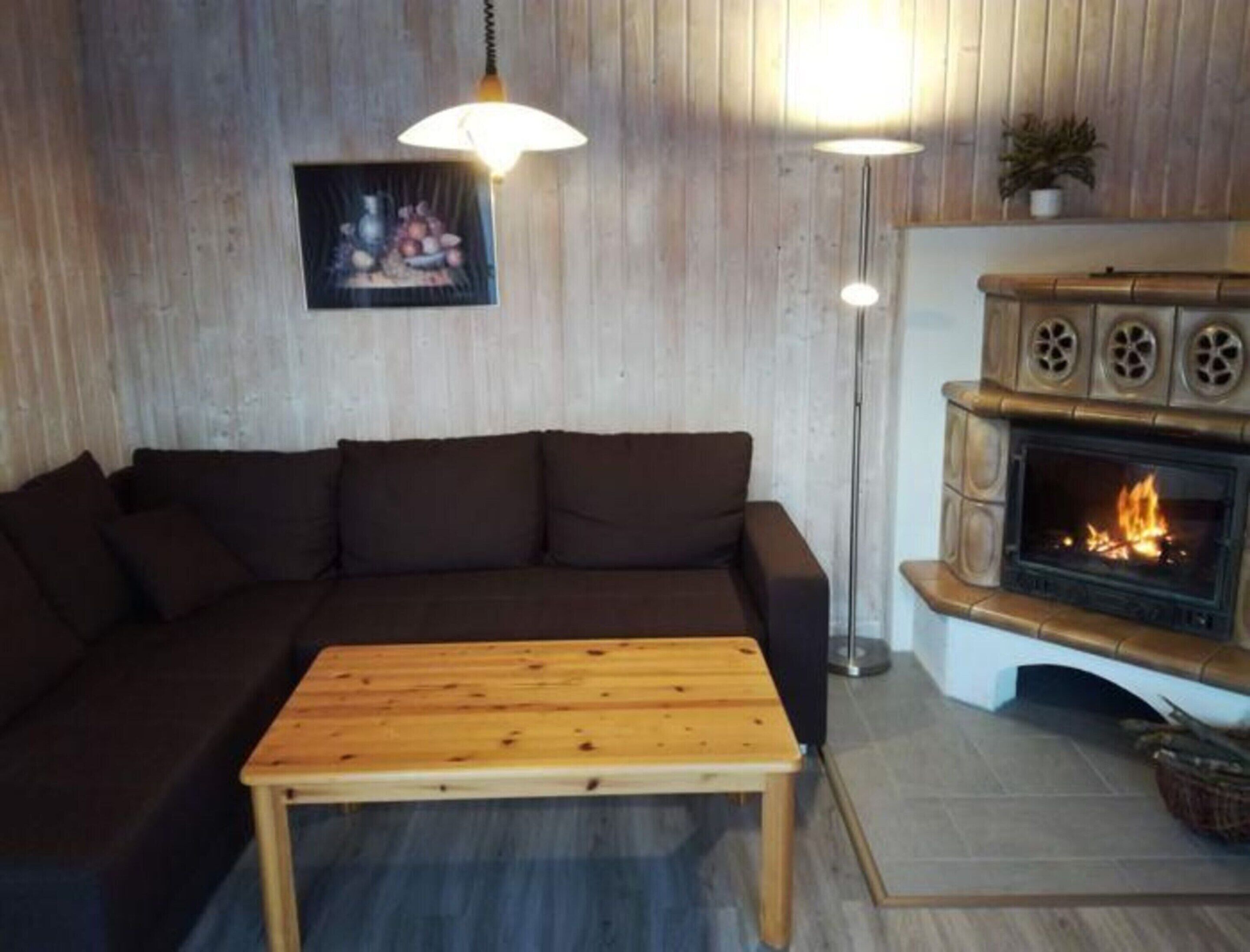 A cozy living room with a wooden sofa, a wooden coffee table, a fireplace with a visible fire, and two pendant lights.