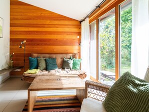 A cozy room with a wooden ceiling, a large window, a sofa with cushions, a table with glasses, and a wicker chair. - Holiday Home in Allrode With Garden (Thale)
