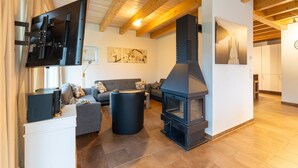 Uma sala de estar moderna com lareira, vigas de madeira, um sofá e uma TV de tela plana.