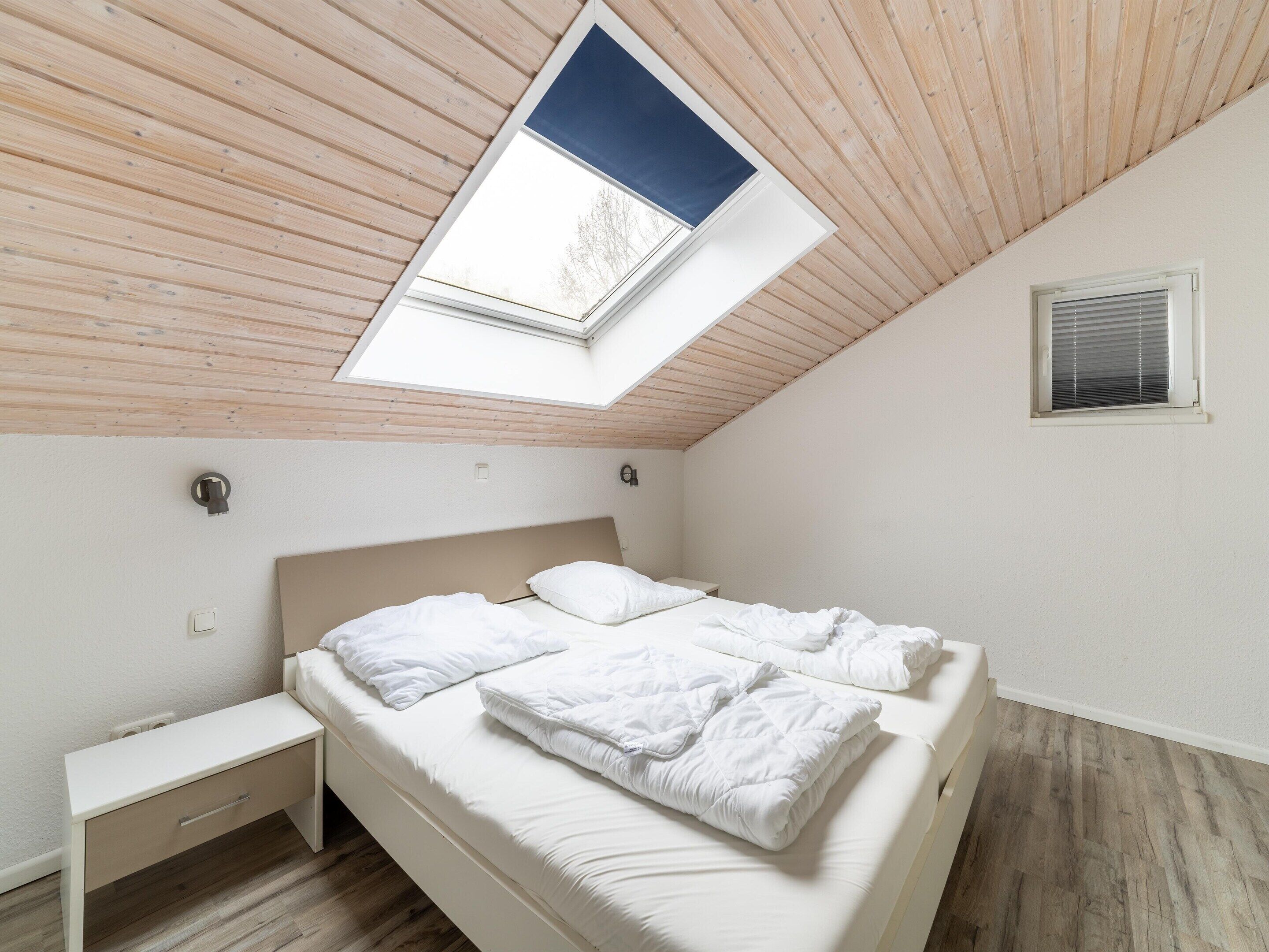 Ein Schlafzimmer mit Oberlicht, einem Bett, einem Nachttisch und einem Fenster mit Jalousien.