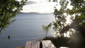A wooden picnic table with a metal cup, overlooking a calm lake with distant hills. - 5 Star Holiday Home in Sorbovag (Hyllestad)