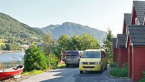 A yellow van parked in front of a building with a red roof, a body of water, and mountains in the background. - 5 Star Holiday Home in Sorbovag (Hyllestad)