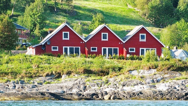 A coastal house with a red facade, situated on a rocky shoreline with a view of the sea. - 5 Star Holiday Home in Sorbovag (Hyllestad)