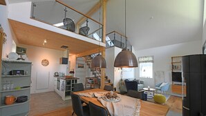 A spacious loft-style living area with a wooden dining table, black chairs, and a staircase leading to an upper level. - Ferienhaus in Schlagsdorf auf Fehmarn (Fehmarn)