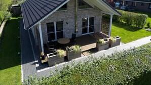 A two-story house with a sloped roof, large windows, and a covered patio area with outdoor furniture. - Ferienhaus in Schlagsdorf auf Fehmarn (Fehmarn)