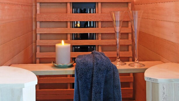 A wooden sauna with a bench, a lit candle, and two glasses on a table. - Ferienhaus in Schlagsdorf auf Fehmarn (Fehmarn)