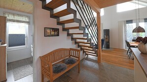 A modern interior with a wooden staircase, a bench with fluffy cushions, and a dining area with a table and chairs. - Ferienhaus in Schlagsdorf auf Fehmarn (Fehmarn)