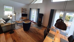 A modern living room with a sofa, a coffee table, a TV, and a dining area with a table and chairs. - Ferienhaus in Schlagsdorf auf Fehmarn (Fehmarn)
