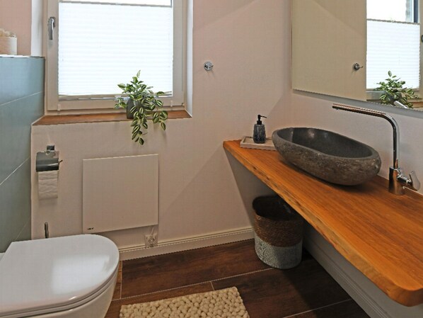 Une salle de bain moderne avec un lavabo en pierre, un meuble-lavabo en bois, des toilettes et un radiateur.