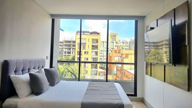 A modern bedroom with a large window, a bed, and a mounted TV. - Urban Chico by Weeki (Bogotá)