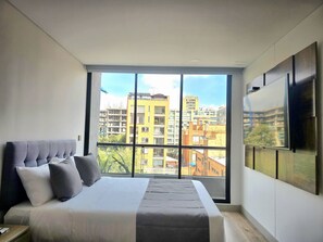 A modern bedroom with a large window, a bed, and a mounted TV. - Urban Chico by Weeki (Bogotá)