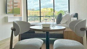 A modern room with a round table, two chairs, a sofa, and a large window offering a city view. - Urban Chico by Weeki (Bogotá)
