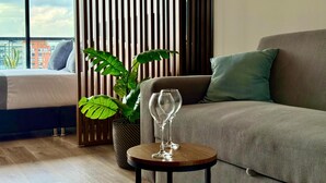 A modern hotel room with a bed, a sofa, a small round table with a wine glass, and a large plant. - Urban Chico by Weeki (Bogotá)