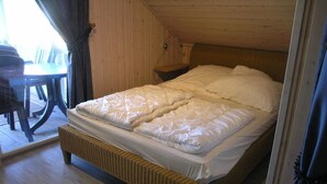 A room with a wooden bed, a wicker bench, and a table with chairs. - Exklusives Skandinavisches Ferienhaus for 6 (Rechlin)