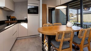 Una cocina moderna con armarios blancos, encimera negra y mesa de comedor de madera con sillas de mimbre.