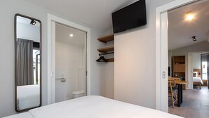Habitación de hotel con cama, televisor montado en la pared, baño con inodoro y ducha, y zona de comedor con mesa y sillas.