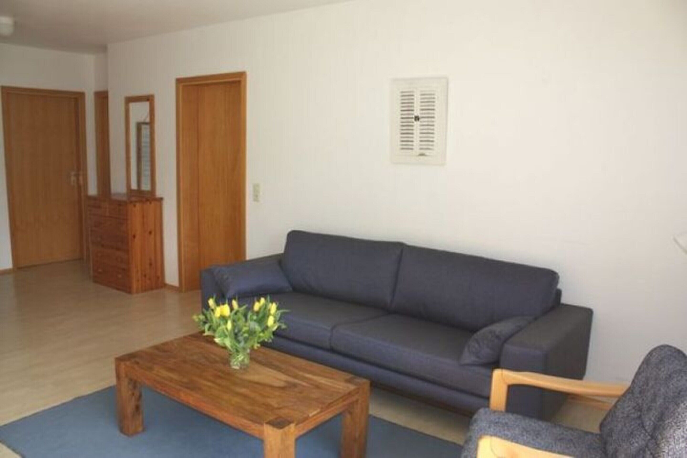 A living room with a dark blue sofa, a wooden coffee table with a vase of flowers, and a wooden chair.