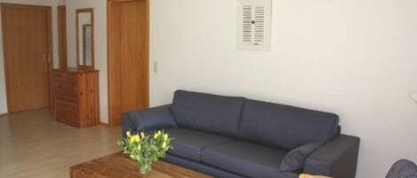 A living room with a dark blue sofa, a wooden coffee table with a vase of flowers, and a wooden chair.
