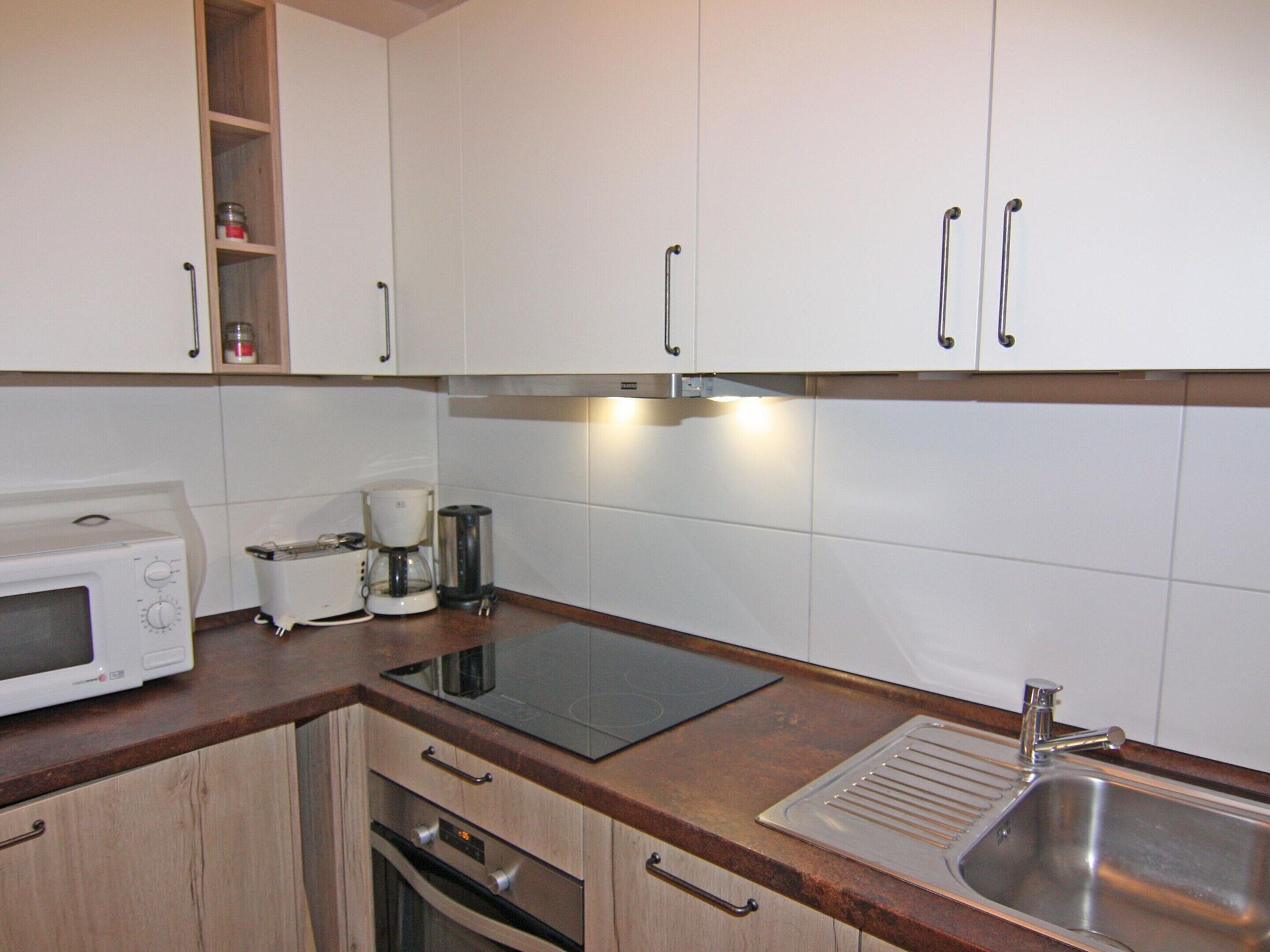 Una cocina con armarios blancos, microondas, cafetera y lavamanos.