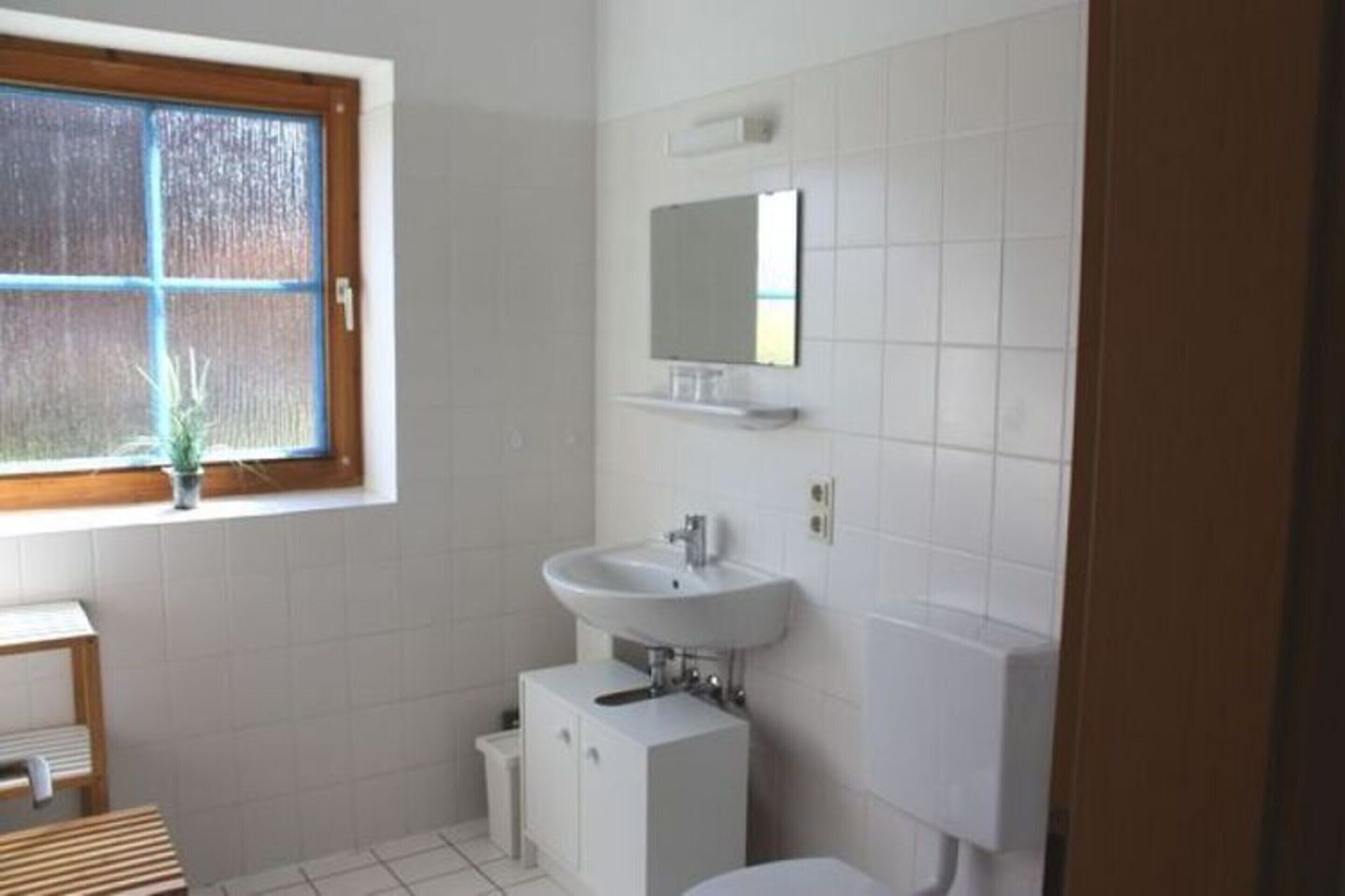 A bathroom with a window, a sink, a mirror, and a toilet.