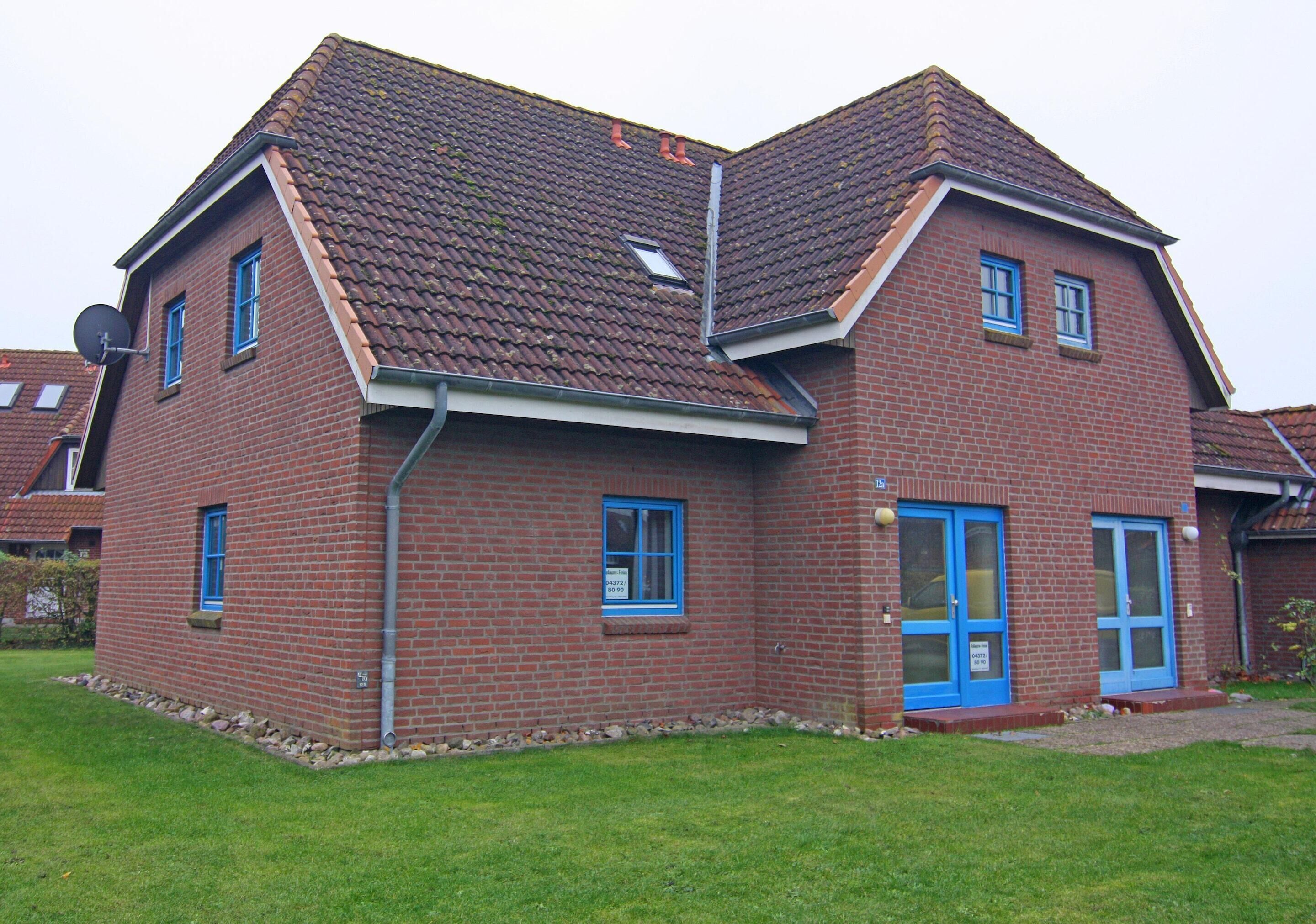 Une maison à deux étages, construite en briques, avec un toit en pente, des fenêtres à cadre bleu et une porte bleue.