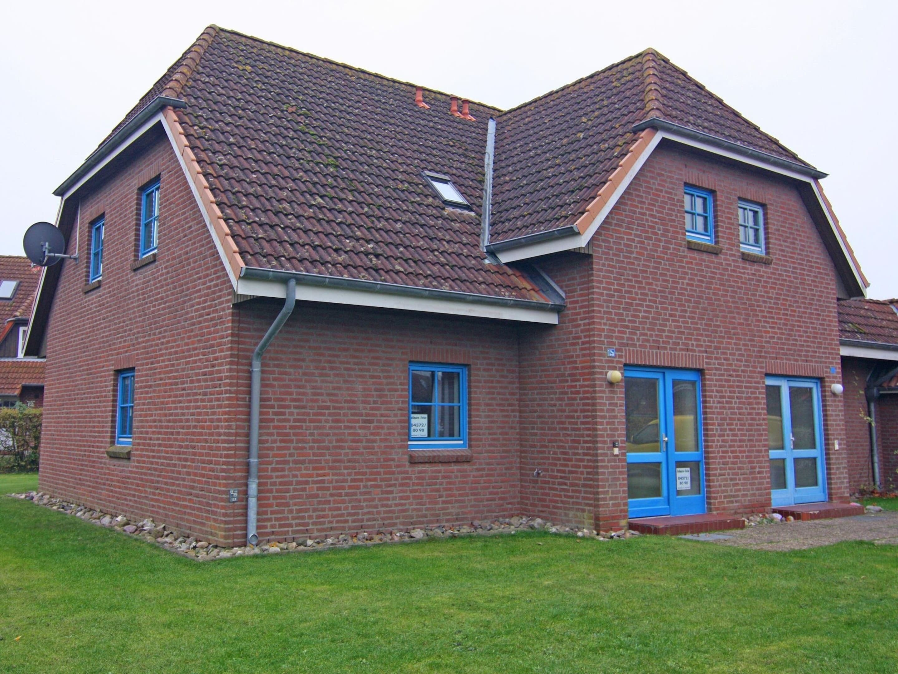 A two-story brick house with a sloped roof, blue-framed windows, and a blue door.