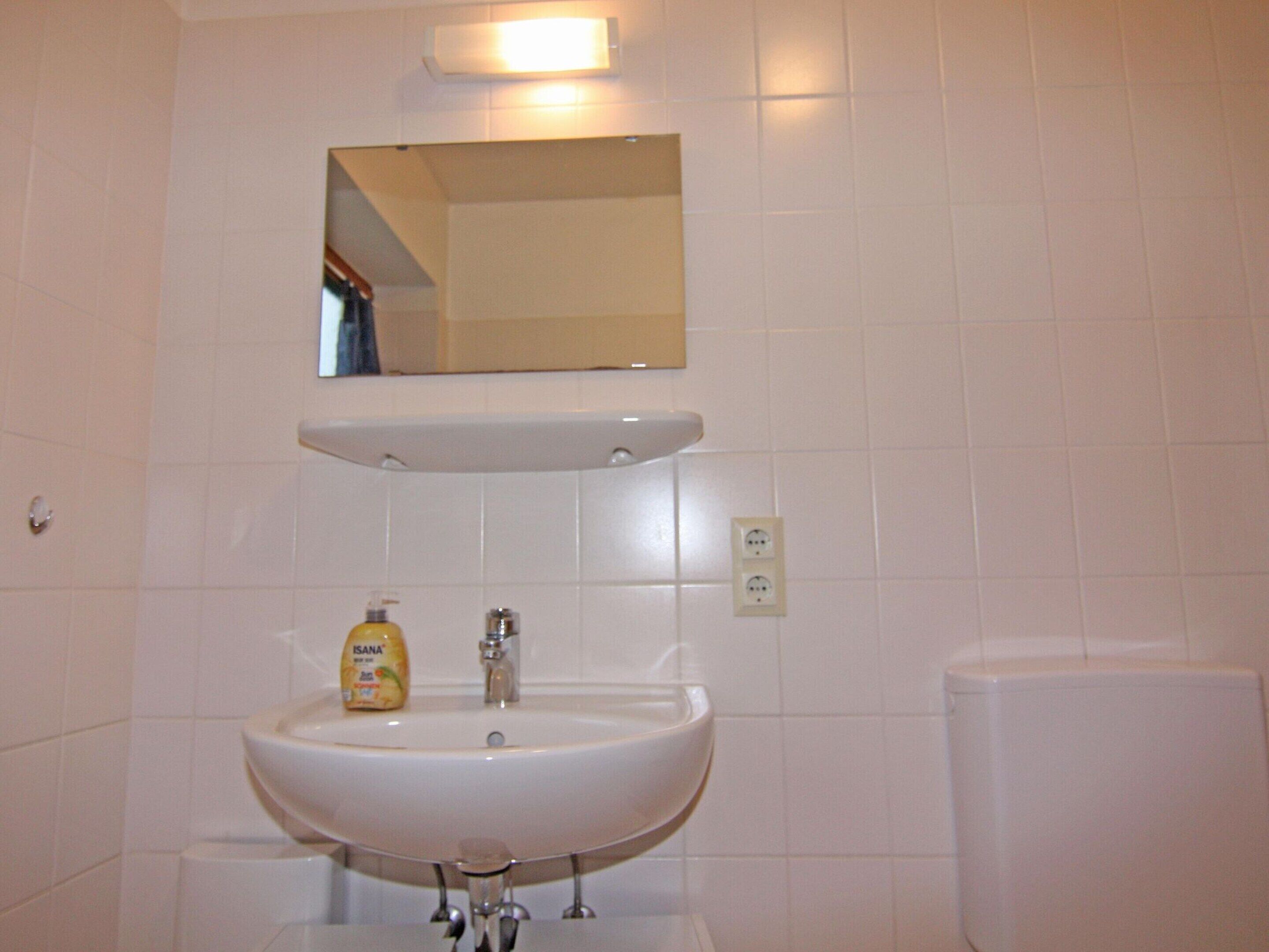Une salle de bain avec un lavabo blanc, un miroir et des murs carrelés.