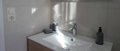 A bathroom with a white sink, a mirror, a wooden cabinet with drawers, and a towel hanging on the wall.
