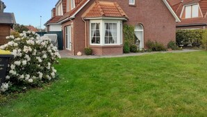 Ett tvåvåningshus med en fasad av tegel, ett tak täckt med takpannor och en liten trädgård framför huset med vita blommor.
