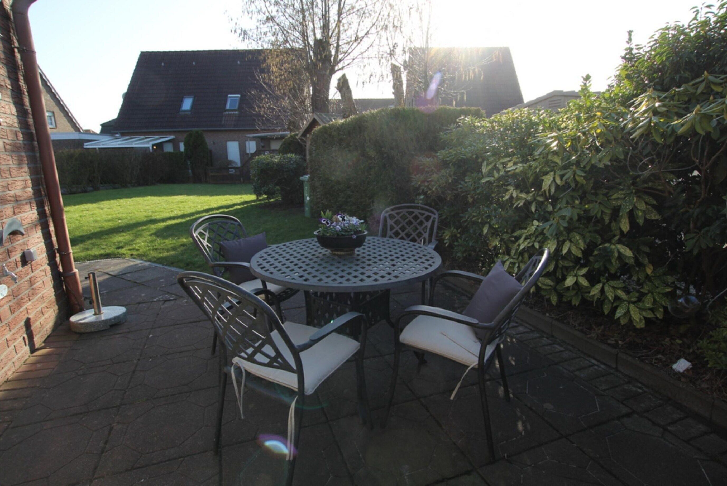 A patio with a round table and four chairs, surrounded by a hedge and a brick wall.