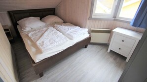 Une chambre à coucher avec un lit en bois, une table de chevet blanche et une fenêtre avec des rideaux.