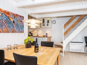Eine moderne Küche mit weißen Schränken, ein Essbereich mit einem Holztisch und eine Treppe, die zu einer weiteren Ebene führt.