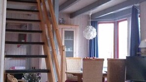 A room with a wooden staircase, a dining table with chairs, a television, and a window with curtains. - Skandinavisches Ferienhaus in Mirow (Mirow)