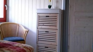 A room with a bed, a wicker chair, a white cabinet with drawers, and a small plant on top. - Skandinavisches Ferienhaus in Mirow (Mirow)