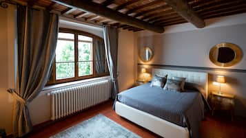 Un dormitorio con una cama grande, dos mesitas de noche con lámparas, una ventana con cortinas, un radiador y un techo de madera.