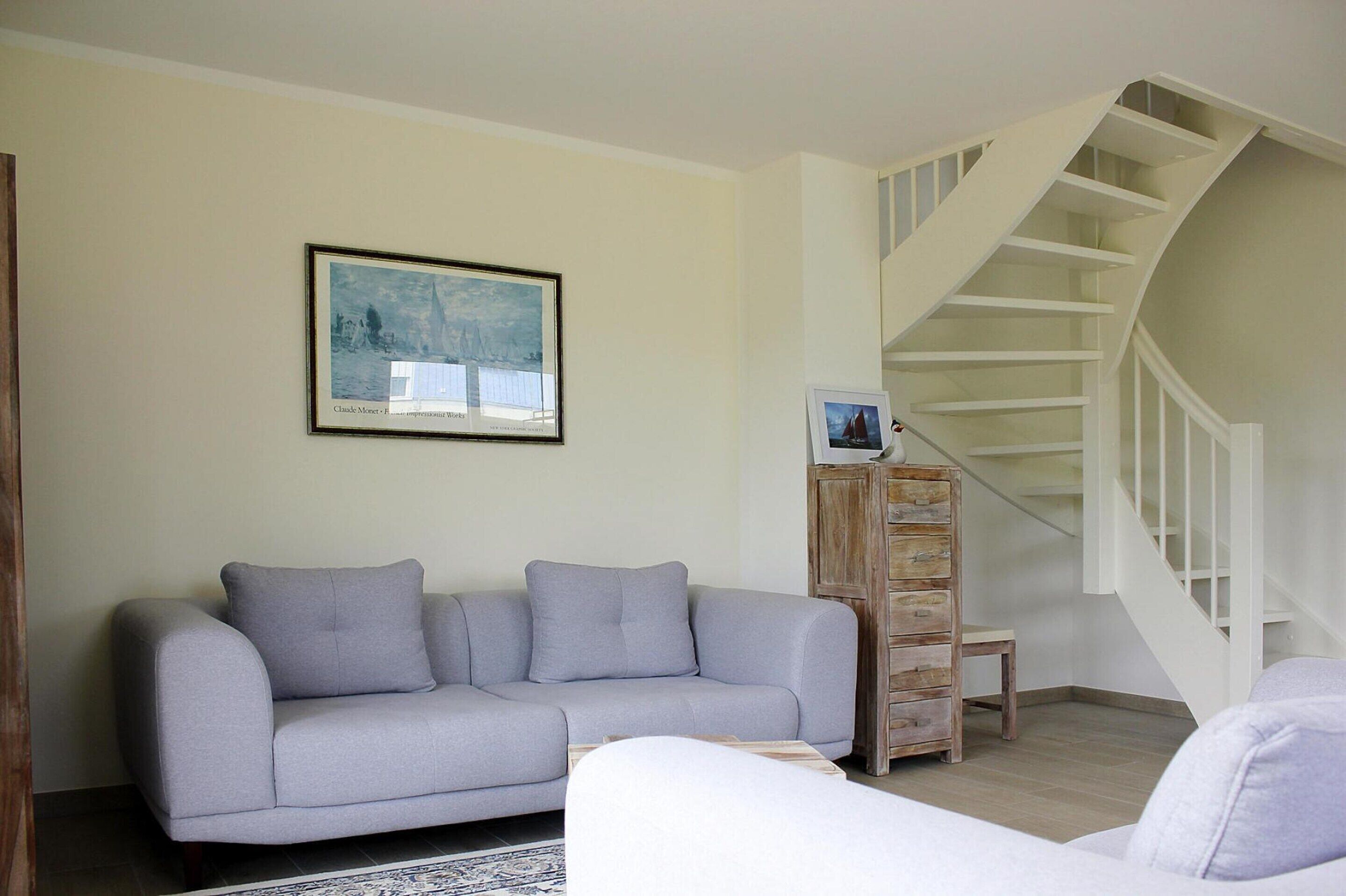 A living room with a grey sofa, a wooden cabinet, and a staircase.