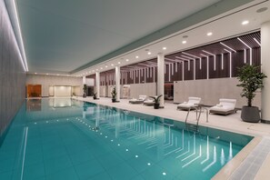 Une piscine intérieure moderne, avec une eau cristalline, entourée de chaises longues et de plantes en pot.