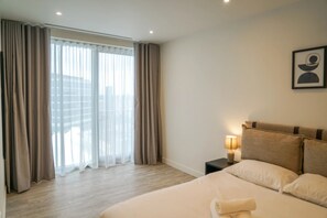 Une chambre d’hôtel avec un grand lit, une table de chevet avec une lampe et une fenêtre avec des rideaux.