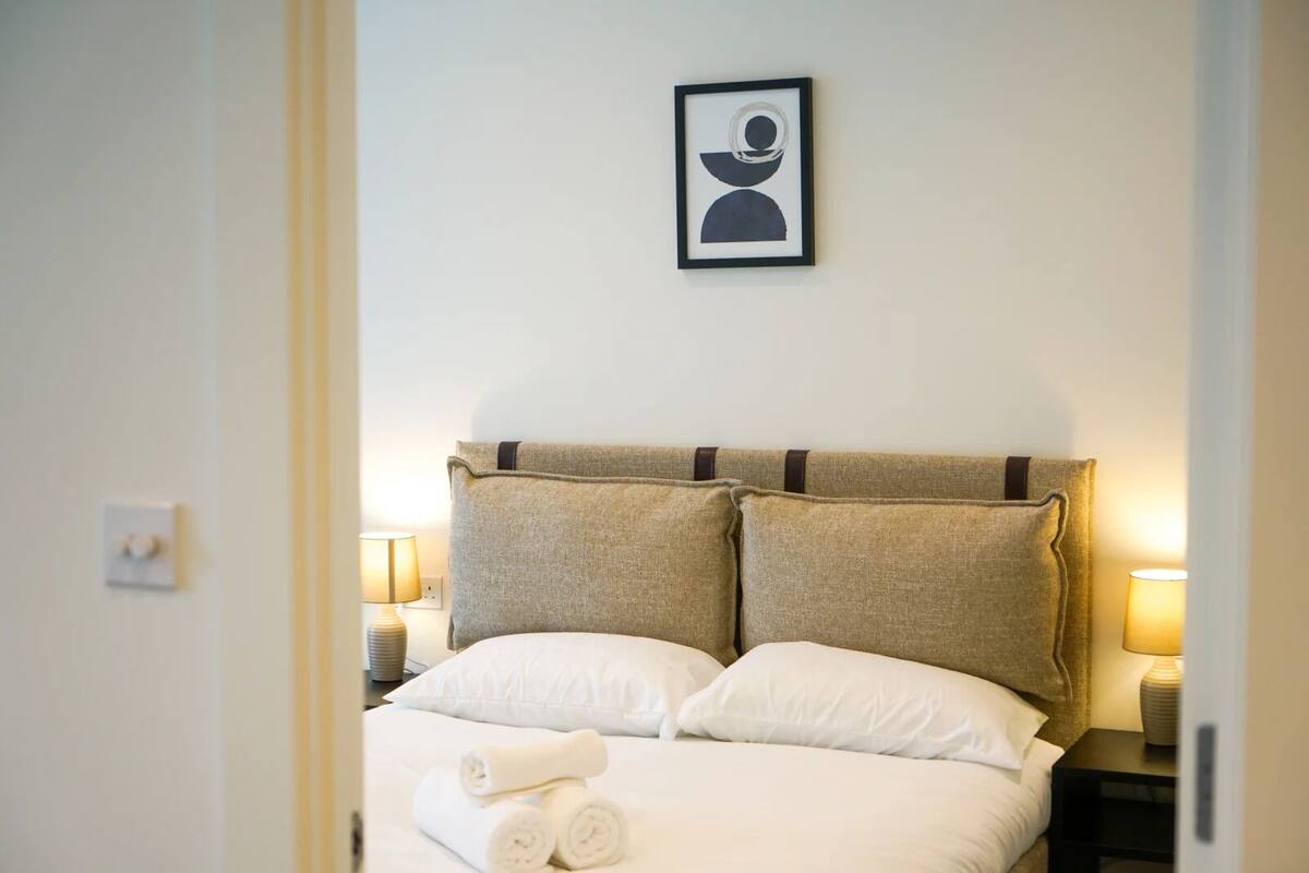 A neatly made bed with two pillows, a framed picture on the wall, and two bedside lamps.