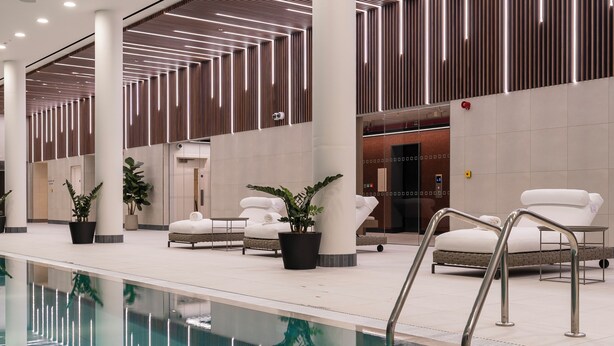 Ein moderner Poolbereich im Innenbereich mit klarem Wasser, Liegestühlen und einem zeitgemäßen Design mit geometrischen Mustern an Decke und Wänden.
