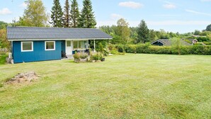 Une maison bleue avec un toit en pente, un porche à l’avant et une pelouse bien entretenue.