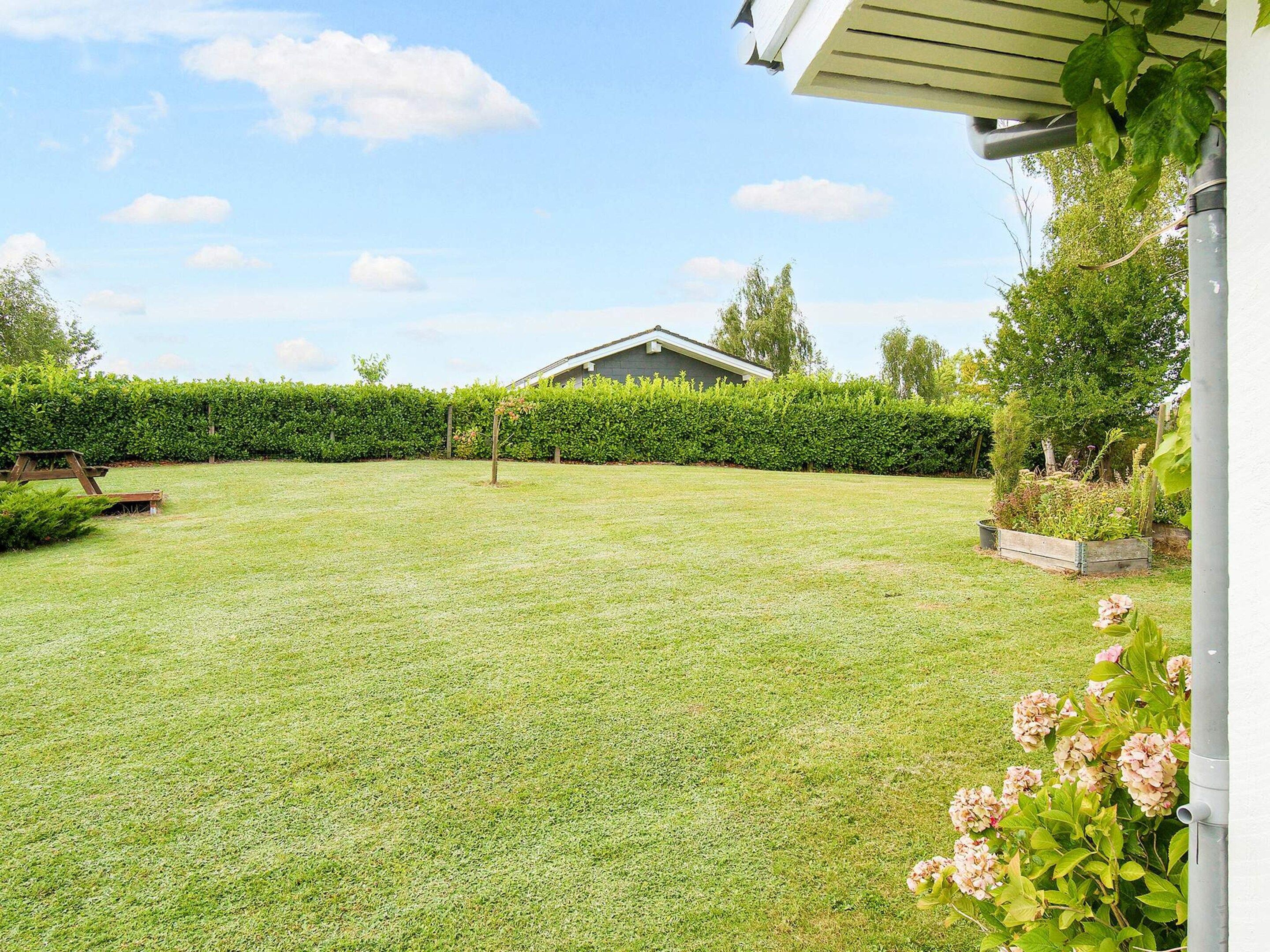 A well-maintained backyard with a lawn, a wooden bench, and a garden bed with flowers.